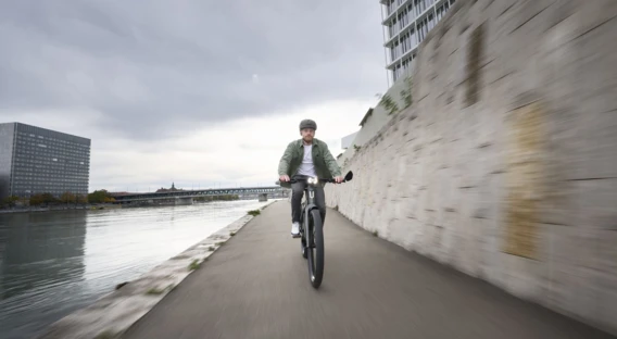 Ein Mann mit Helm fährt auf einem E-Bike vor einer Steinmauer, während der Himmel wolkenverhangen ist.